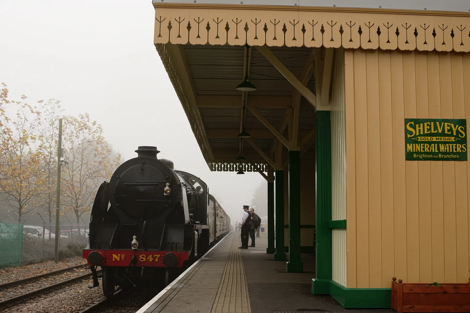 A black steam locomotive numbered 847 arriving beside a yellow wooden station building at East Grinstead