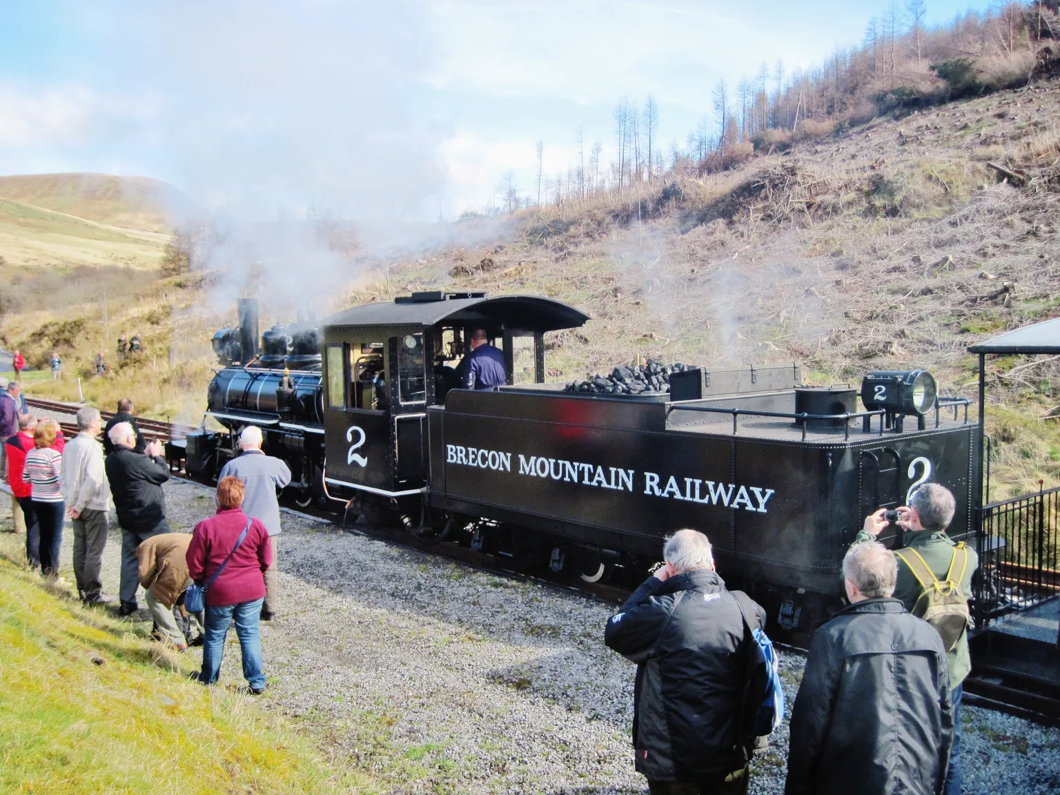Visitors with cameras gathered beside black locomotive No. 2 lettered Brecon Mountain Railway at Torpantau, a bare hillside behind