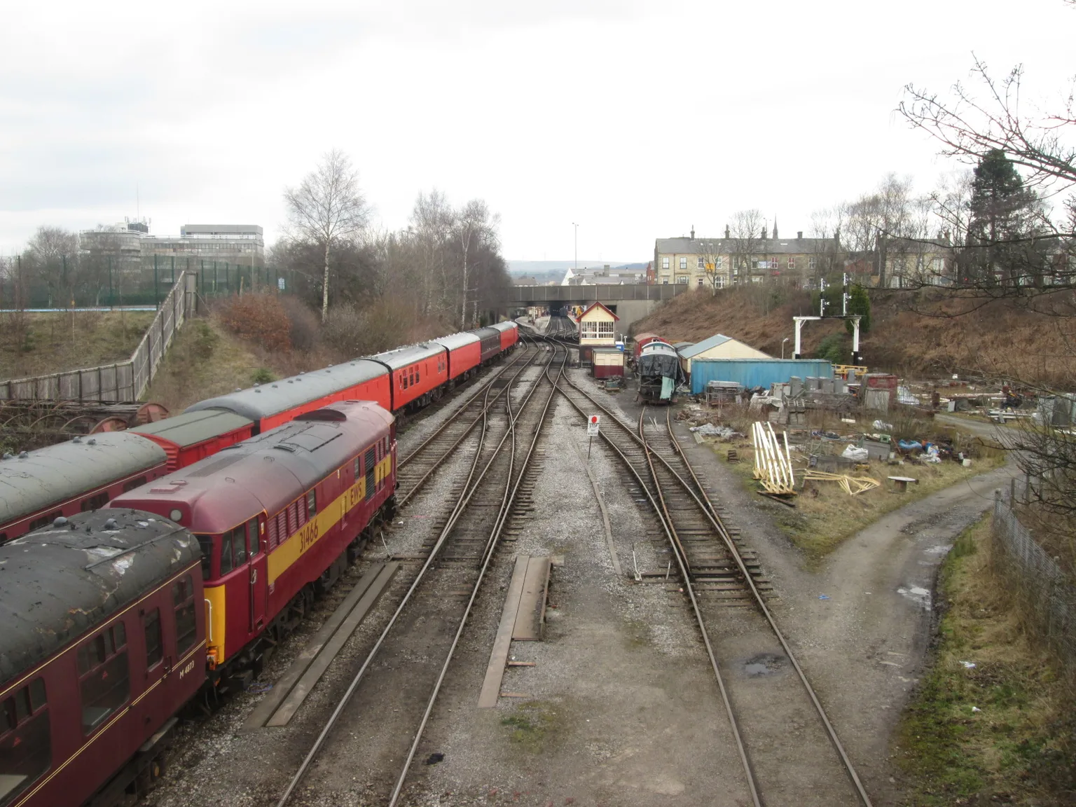 An elevated view along several tracks at Bury, a red and maroon diesel and coaches on the left and the station buildings in the distance