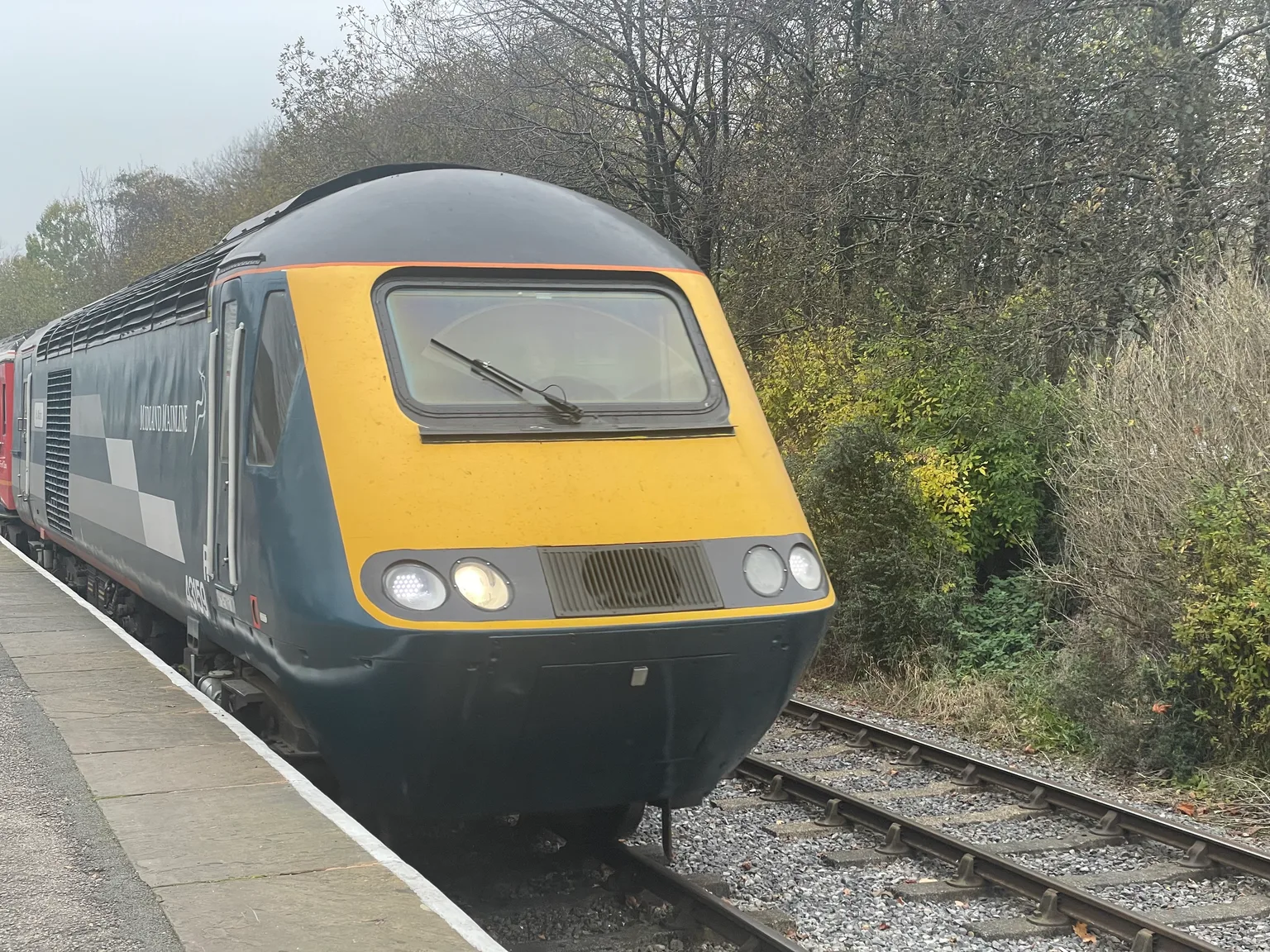 The yellow nose of a diesel high speed train power car numbered 43159 at a platform in Bury, trees behind