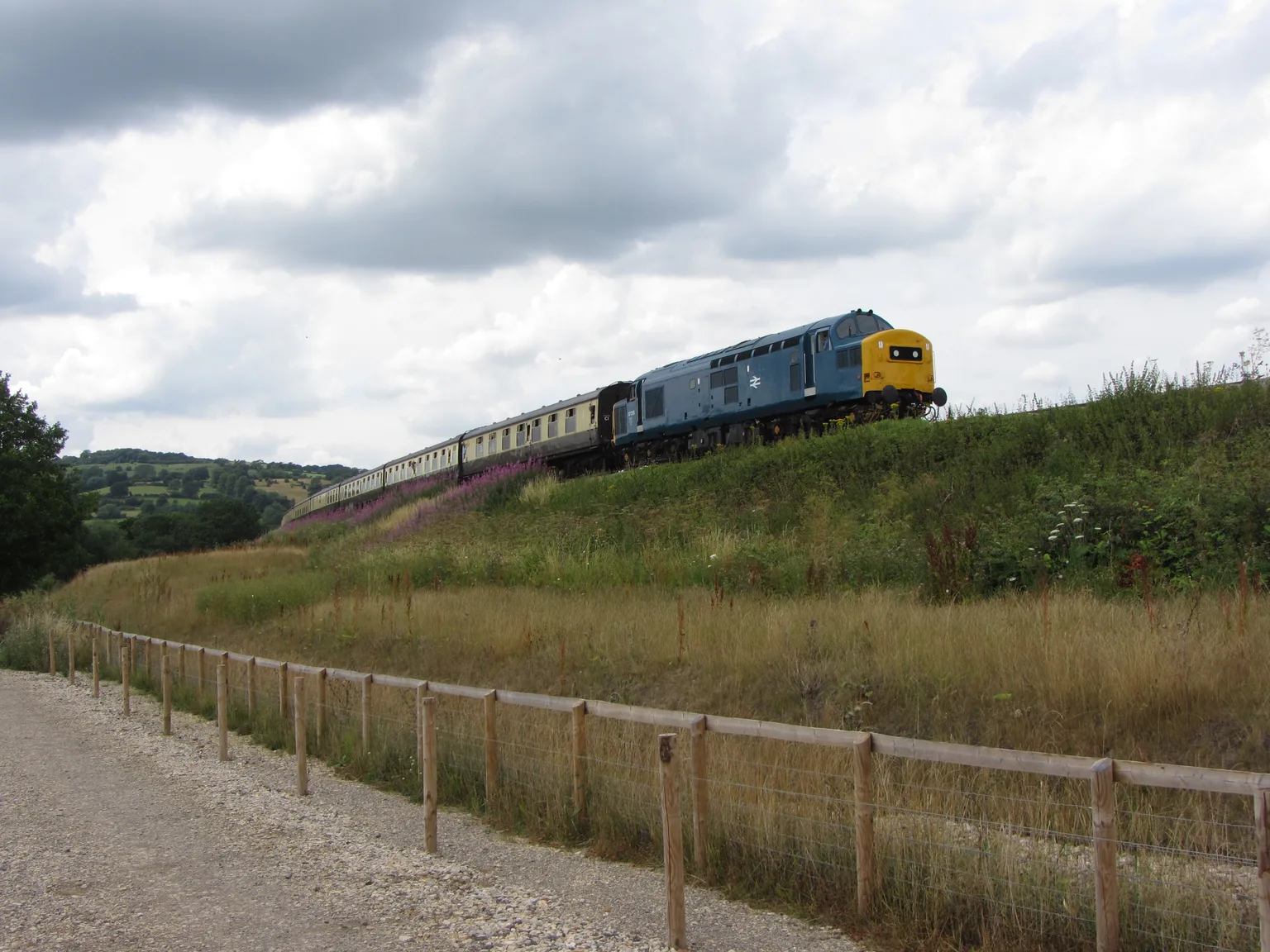 A blue diesel locomotive and carriages on the embankment at Chicken Curve under a cloudy sky