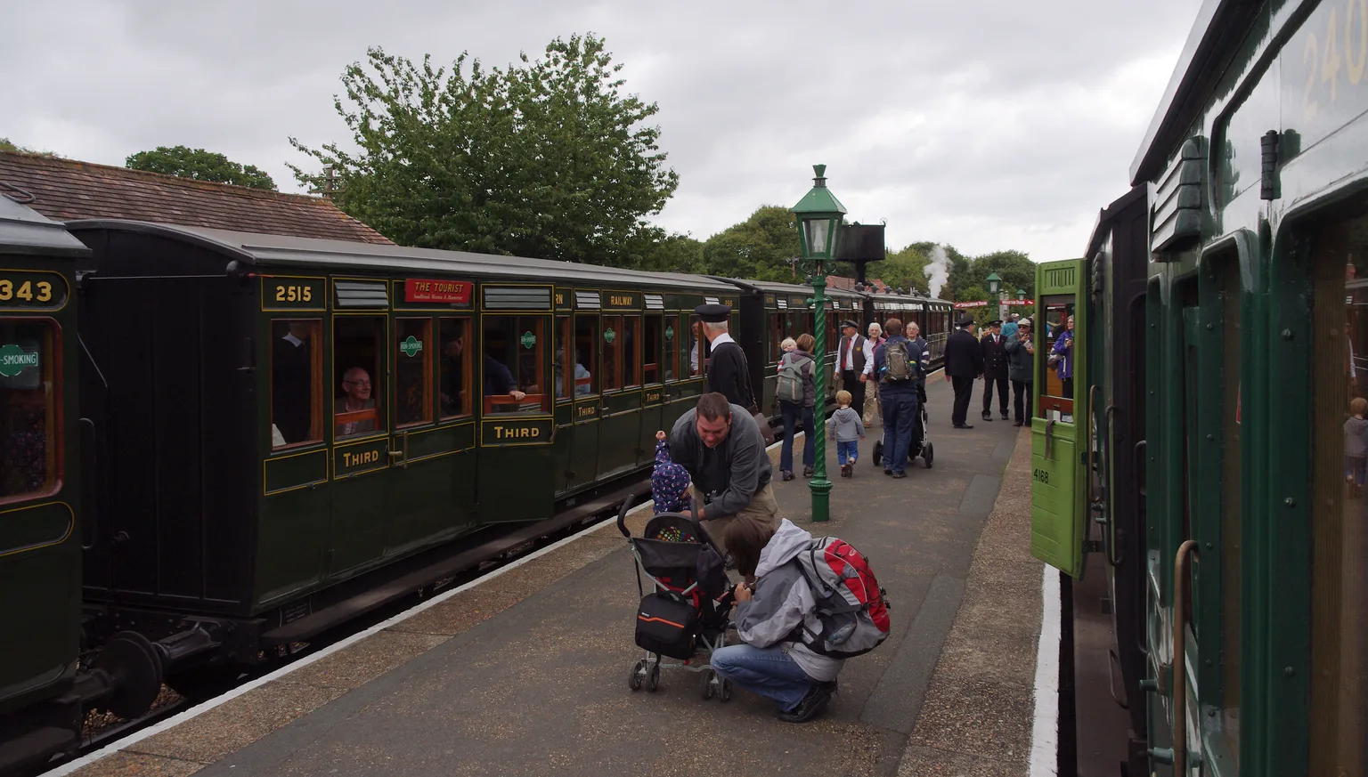 Passengers and staff on the platform at Havenstreet between two trains of dark green wooden carriages