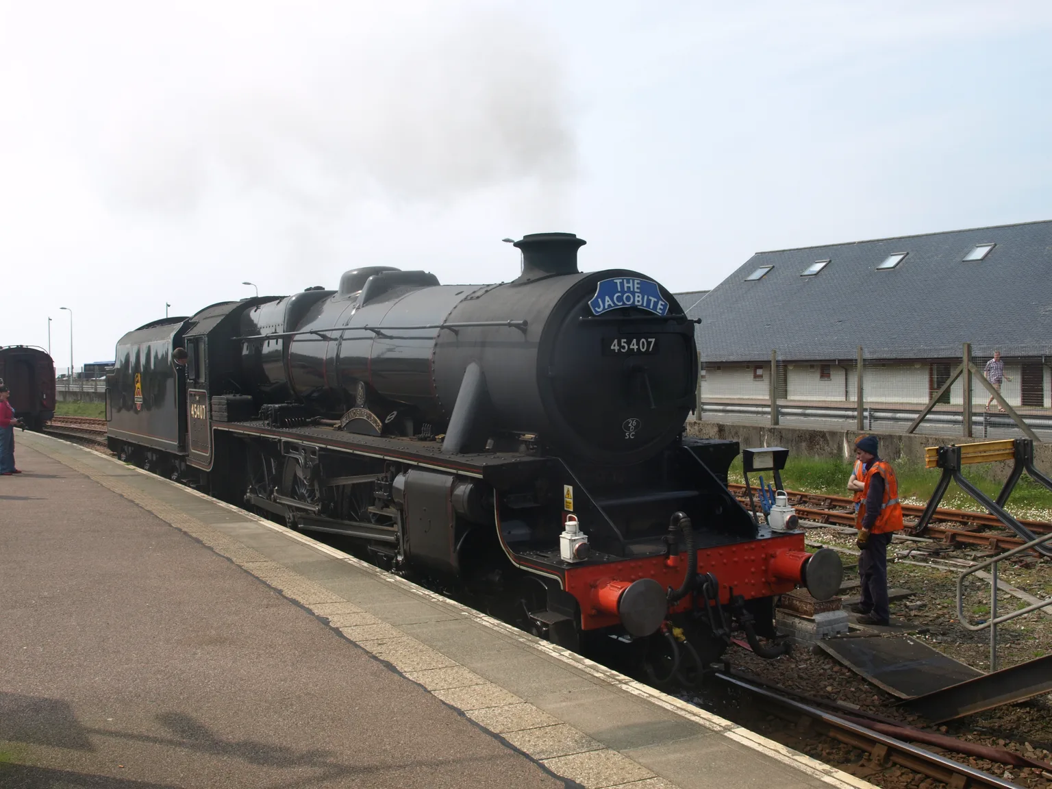 A black steam locomotive with a Jacobite headboard at the platform at Mallaig