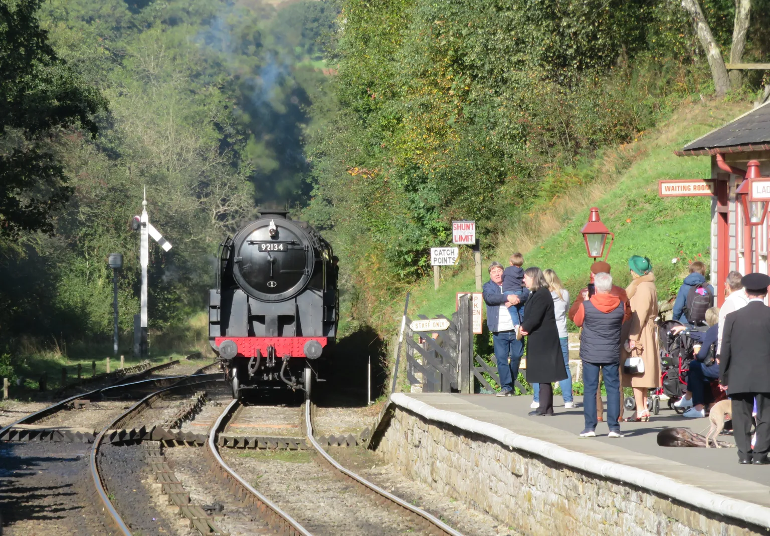A black British Railways steam locomotive arriving at Goathland past the signal, passengers waiting on the platform