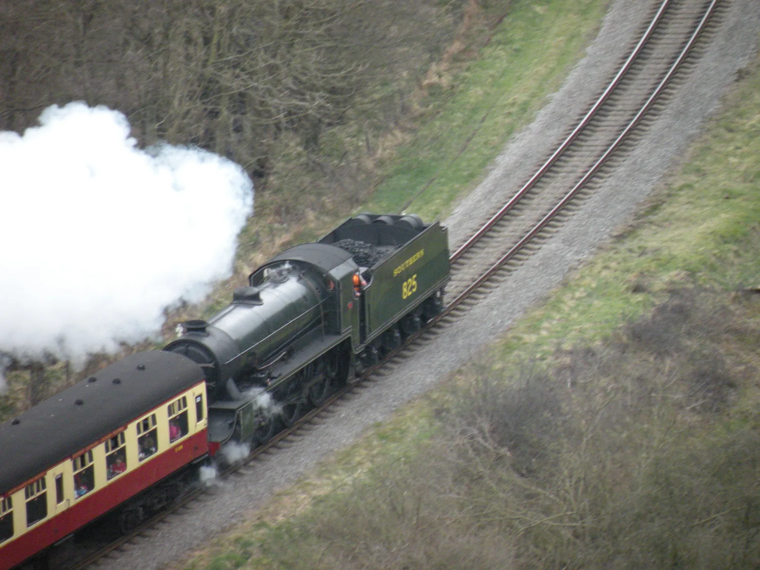 A green steam locomotive and red and cream carriages seen from above as they climb through Newtondale