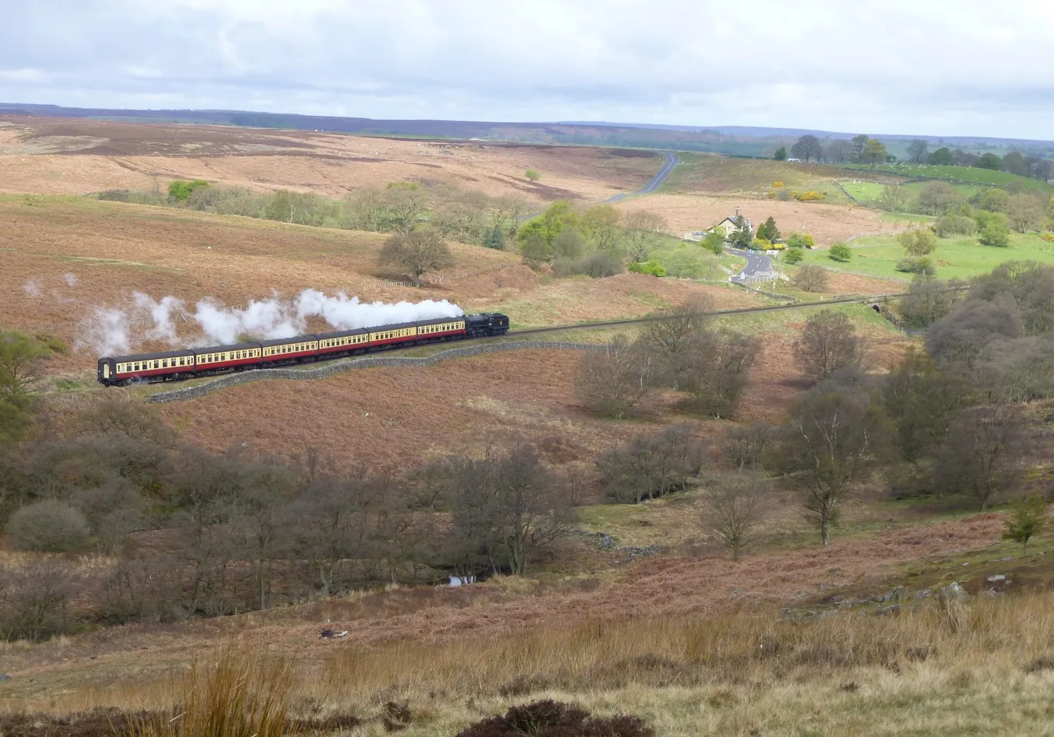 A steam train with red and cream carriages crossing open brown moorland on the North Yorkshire Moors Railway.