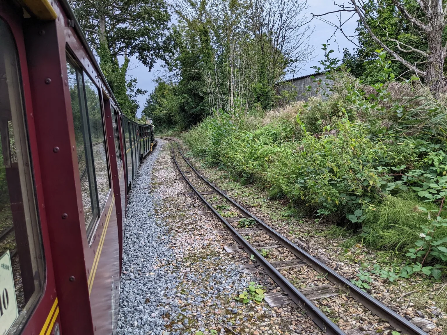 The view from a miniature train window looking ahead along a single track between green banks of trees and bushes