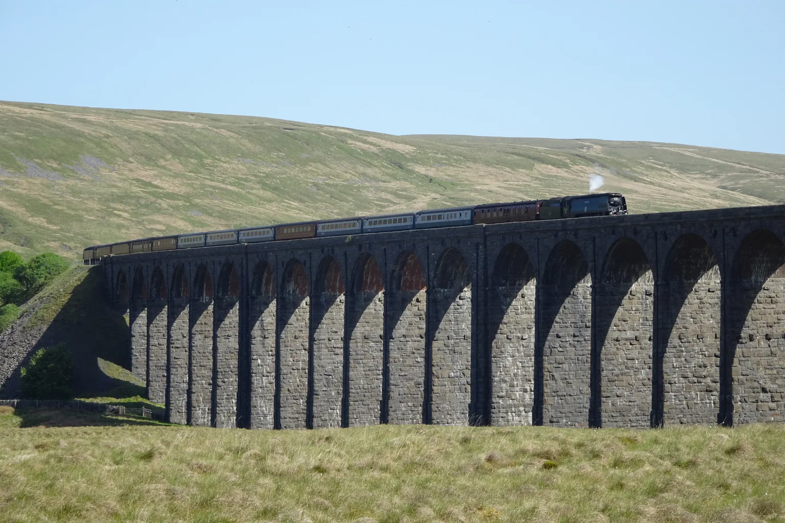 A steam-hauled train crossing the stone arches of Ribblehead Viaduct on the Settle to Carlisle line.