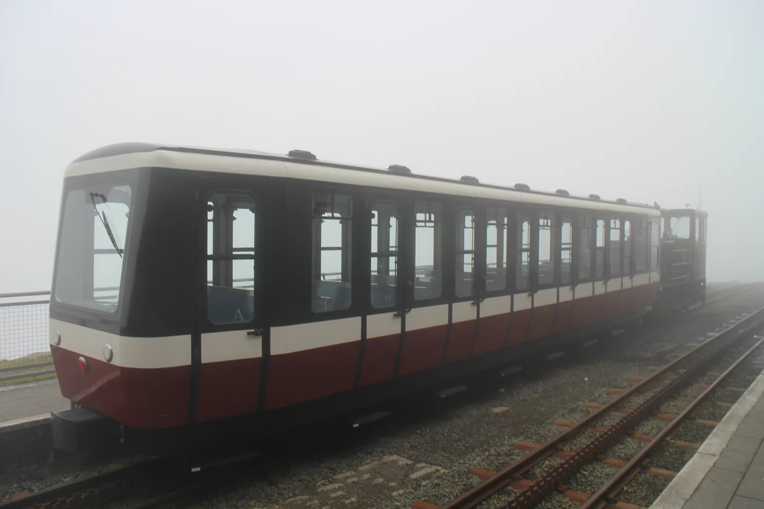 A red and cream carriage and its diesel locomotive standing at a platform in thick fog