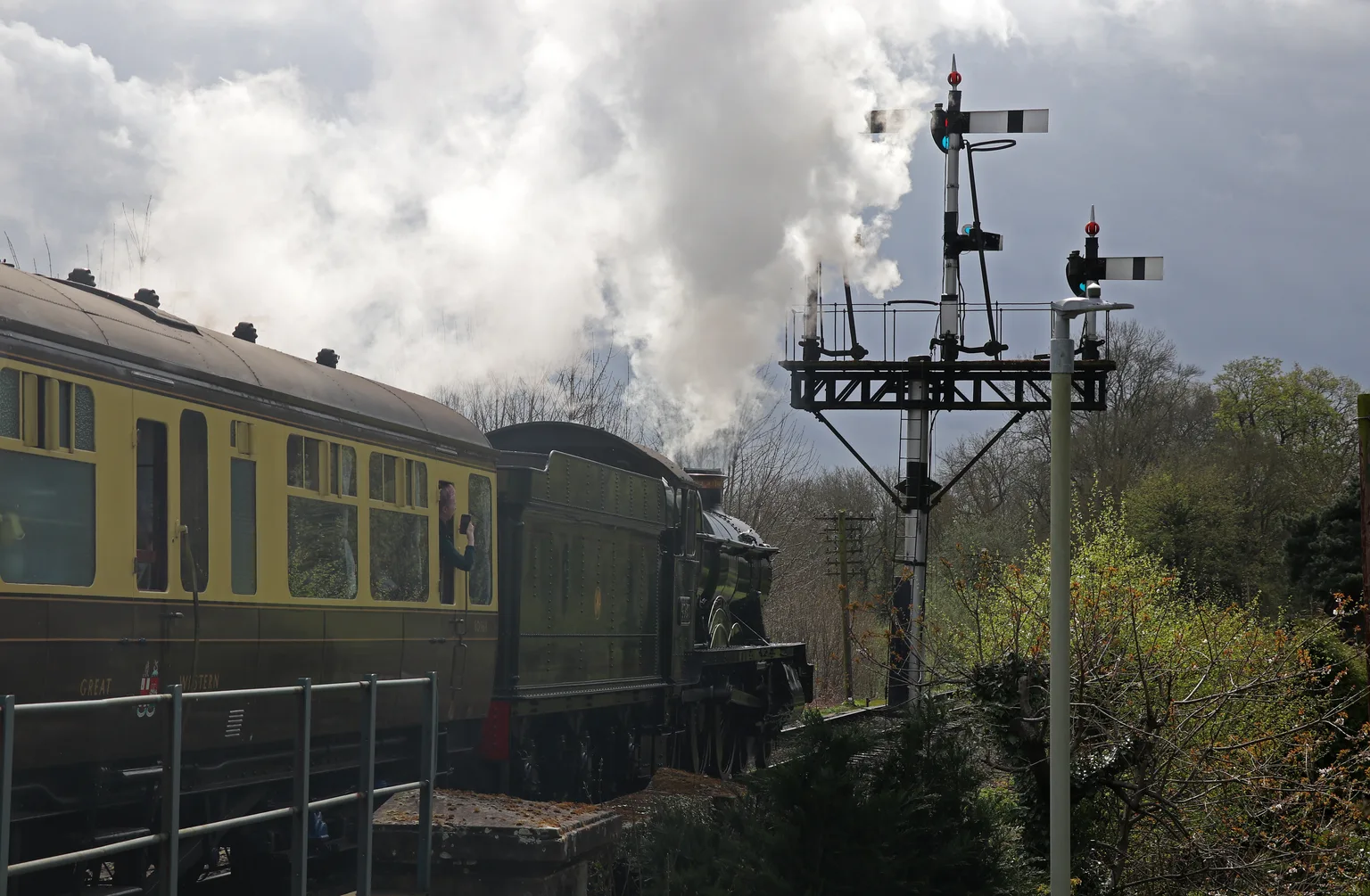 A green steam locomotive leaving Bridgnorth under a tall signal gantry, carriages alongside