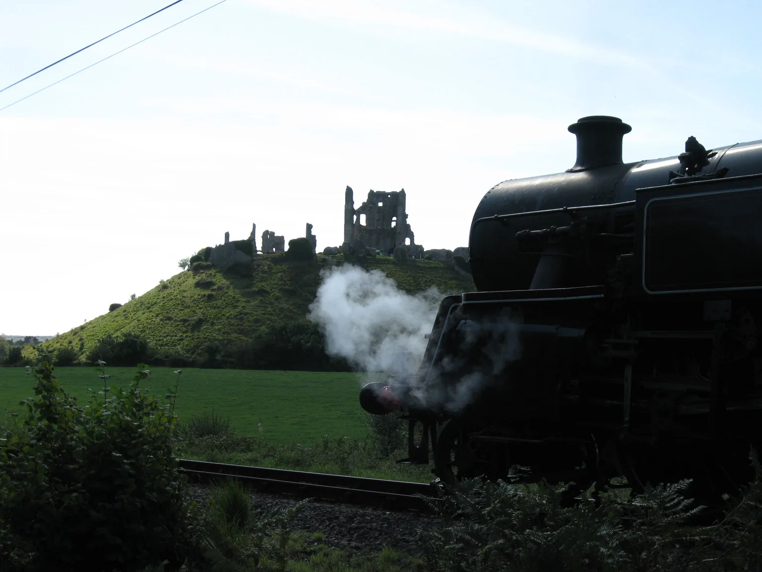 A black steam locomotive in silhouette with the ruins of Corfe Castle on its hill behind.