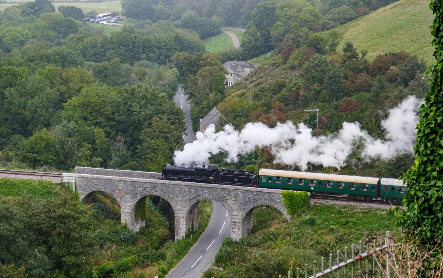 A steam train crossing the stone viaduct below Corfe Castle, steam rolling back over wooded slopes