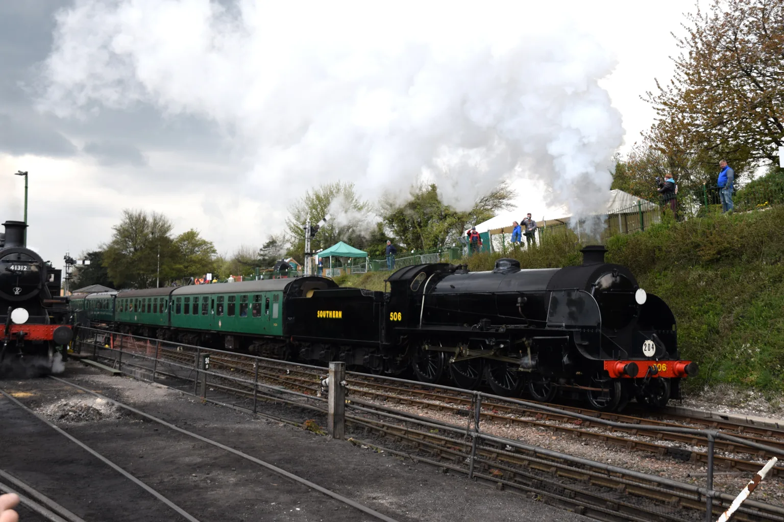 A black steam locomotive numbered 506 departing Ropley with green carriages in a cloud of steam.