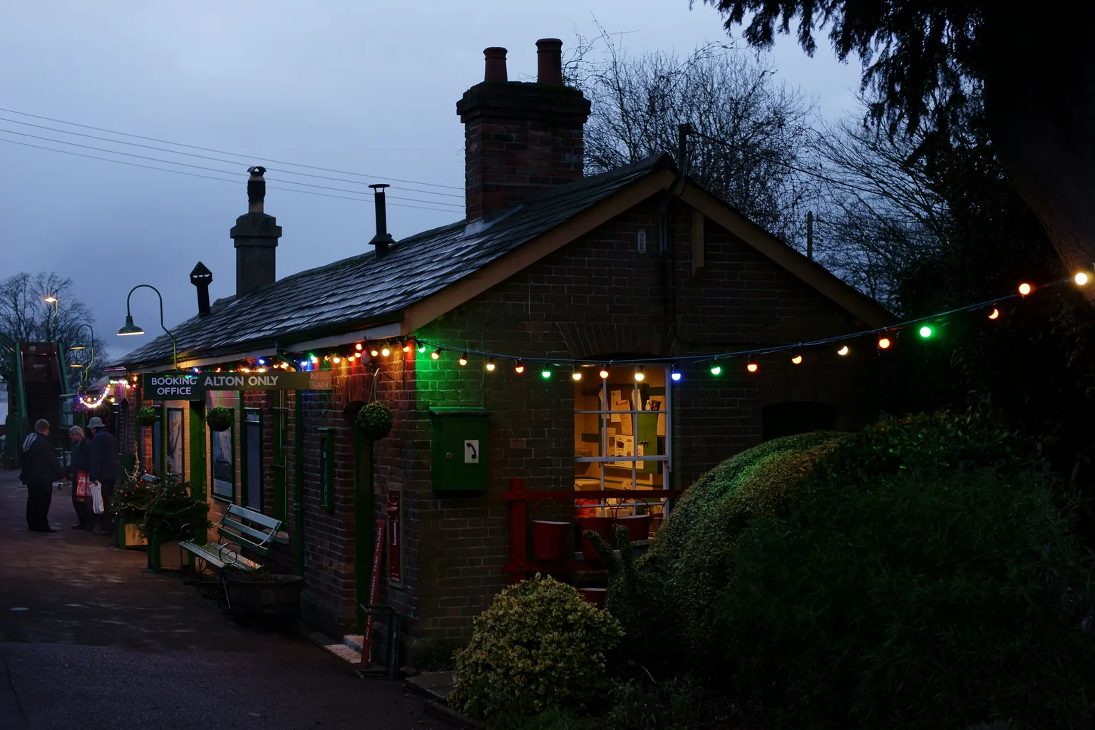 The brick station building at Medstead and Four Marks lit with strings of coloured lights at dusk
