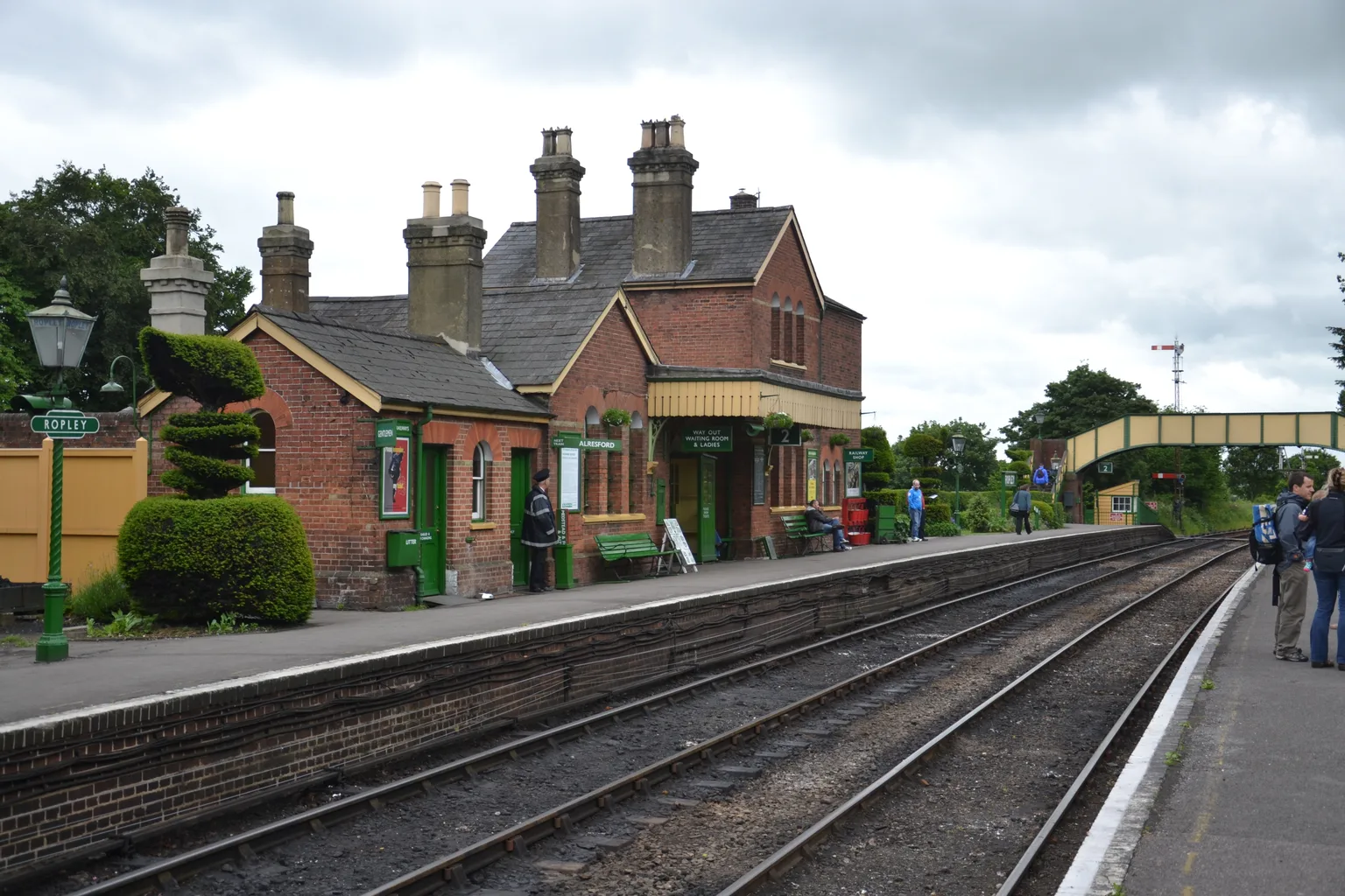 The brick station building and topiary at Ropley, a footbridge beyond the platform