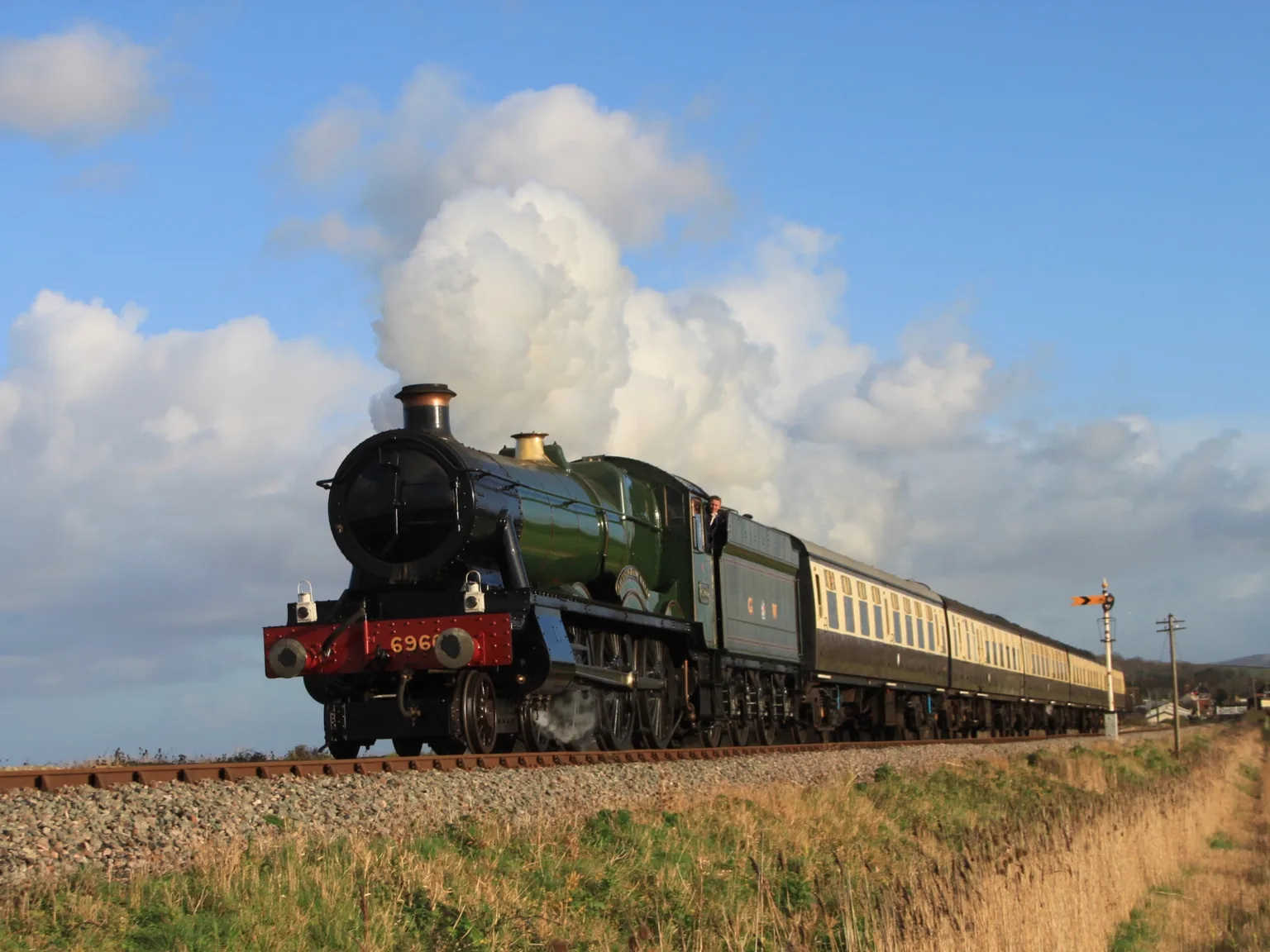 A green steam locomotive with chocolate and cream carriages leaving Blue Anchor under a big white cloud of steam
