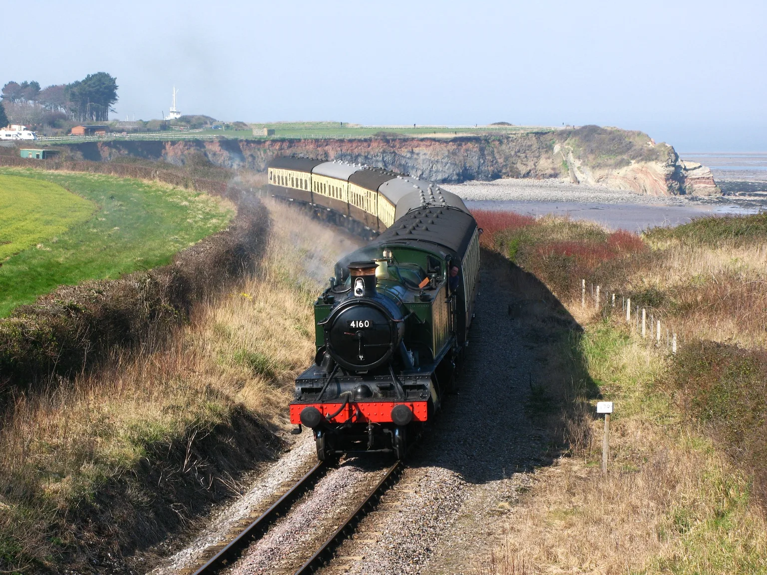 A green tank engine heading a train along the cliff-top curve at Helwell Bay on the Somerset coast.