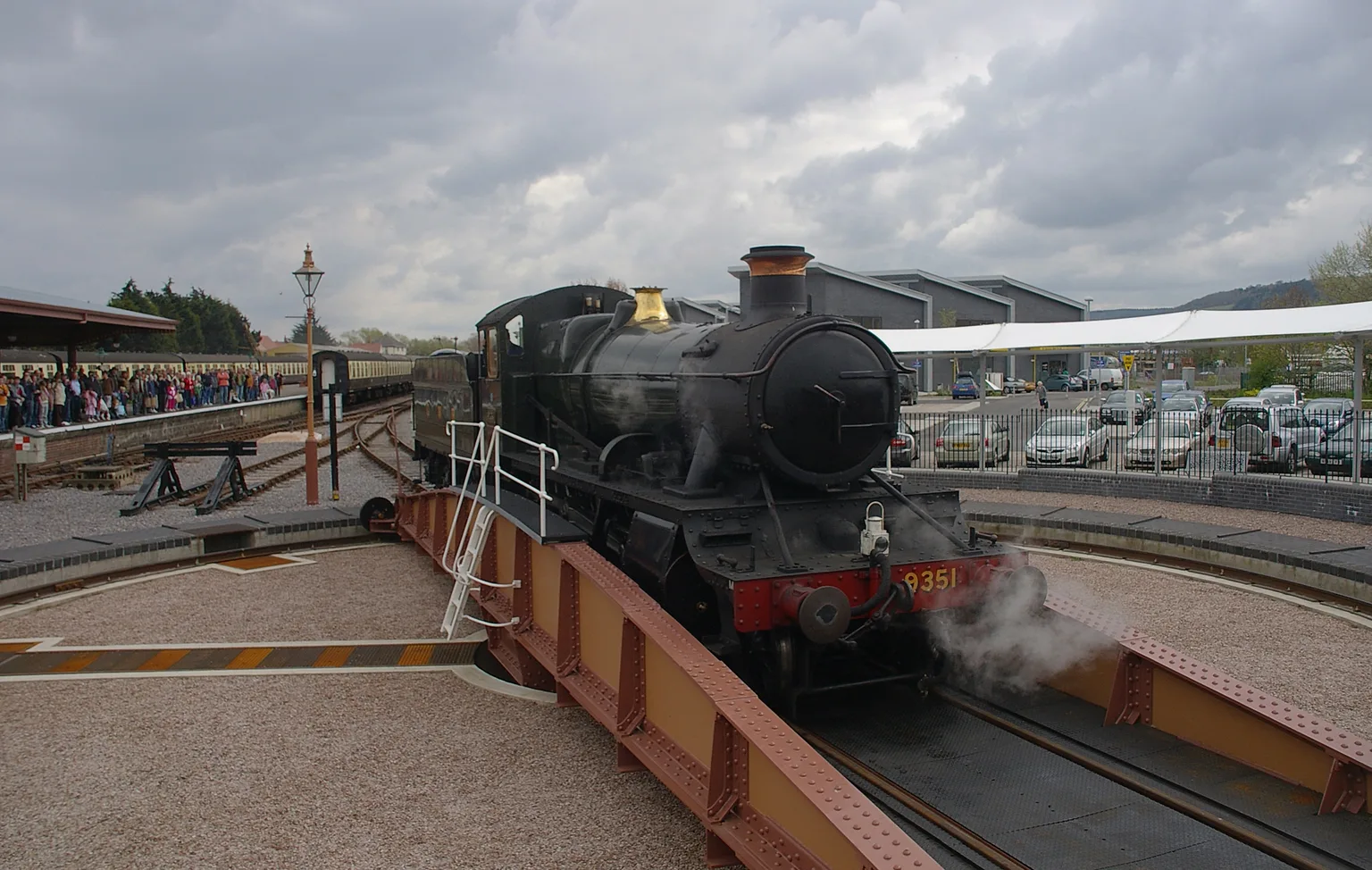 A green steam locomotive numbered 9351 on the turntable at Minehead with spectators behind a fence